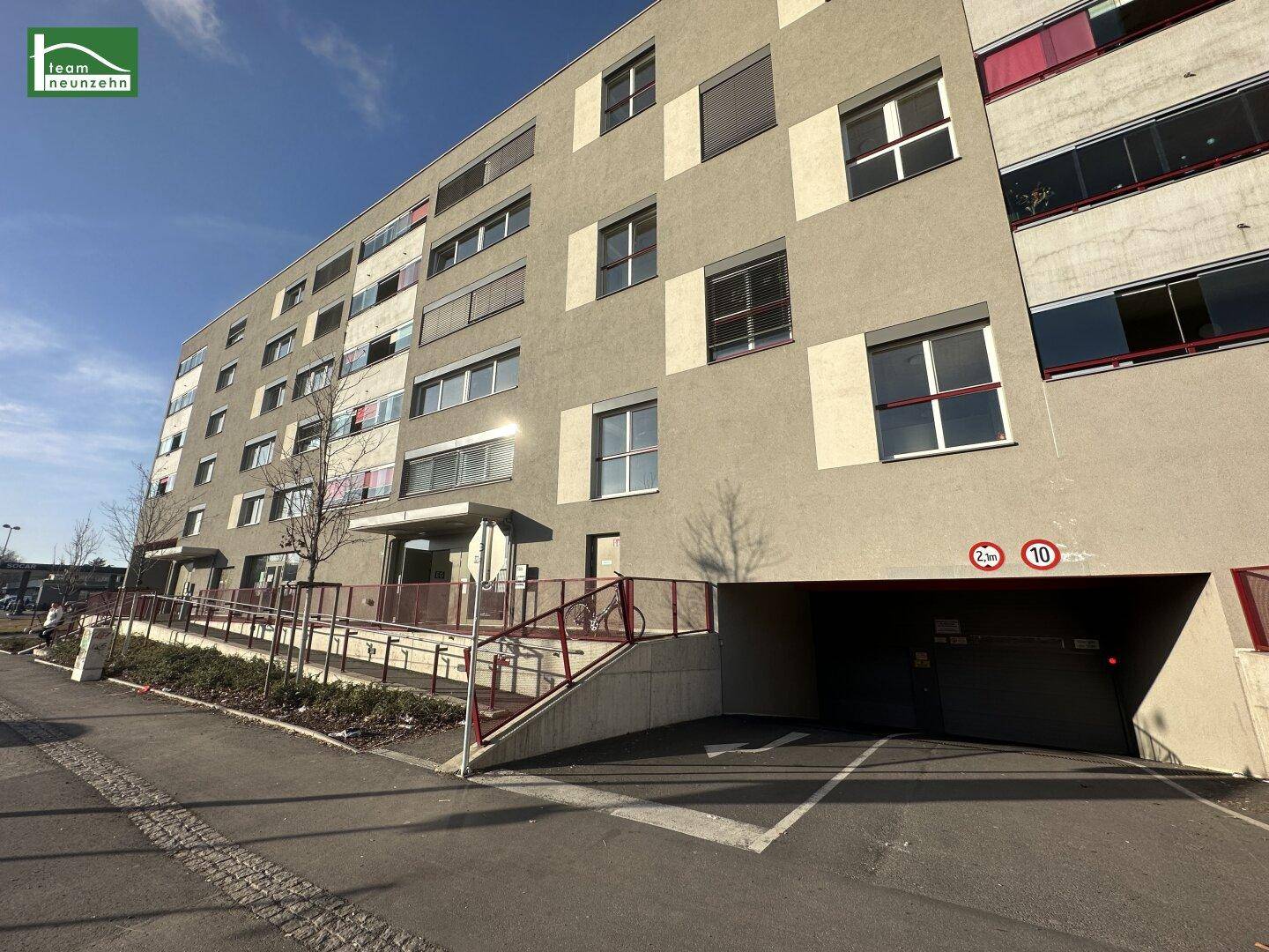 Moderne Gebäudefassade mit Zufahrt zur Tiefgarage und barrierefreiem Zugang über eine Rampe.