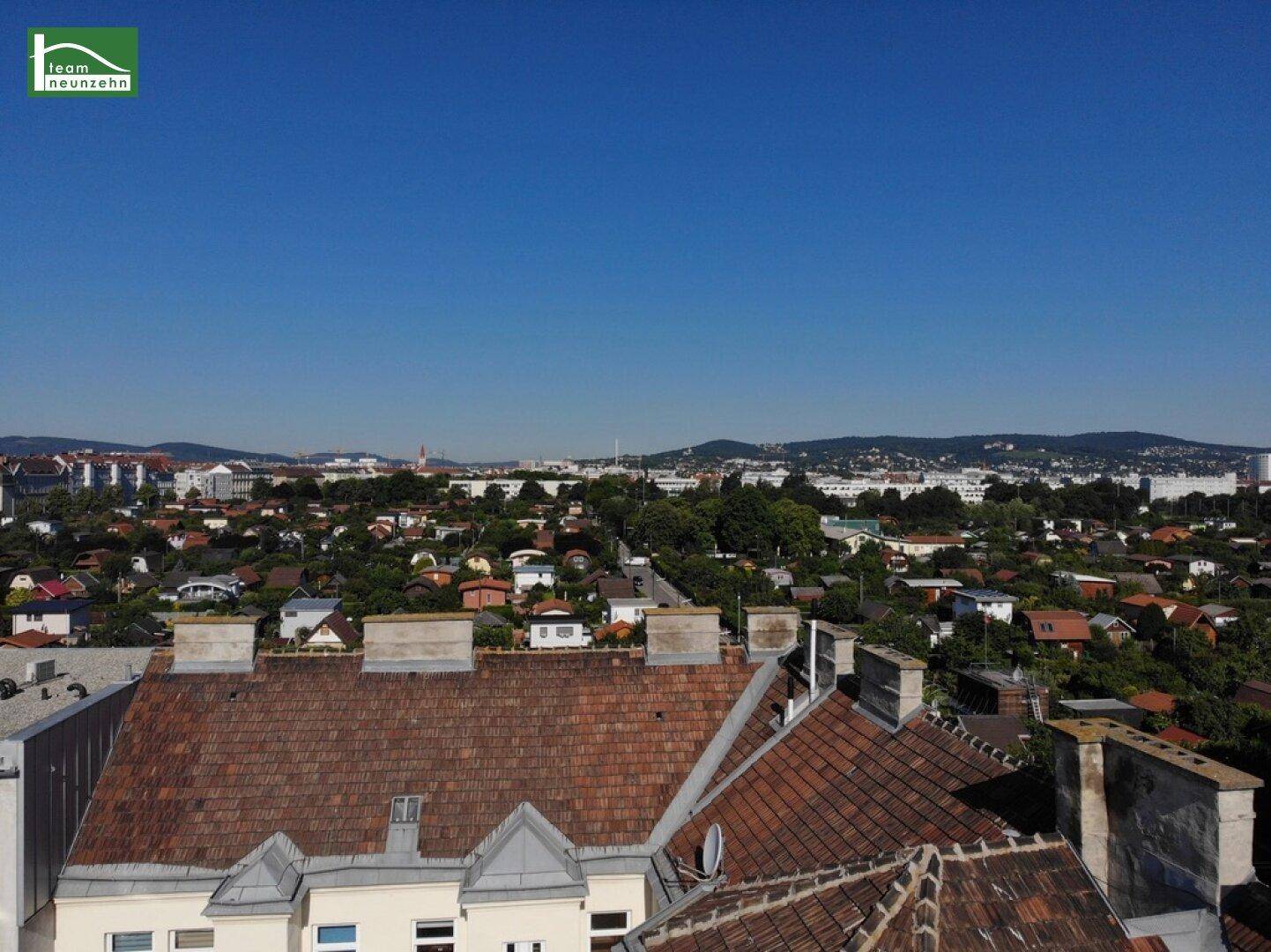 Weitblick über Dächer und grüne Vorstadtlandschaft mit Bergen am Horizont.