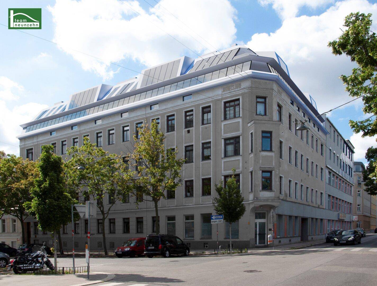 Gebäudeansicht von der Straße mit modernisiertem Dachgeschoss und Bäumen.