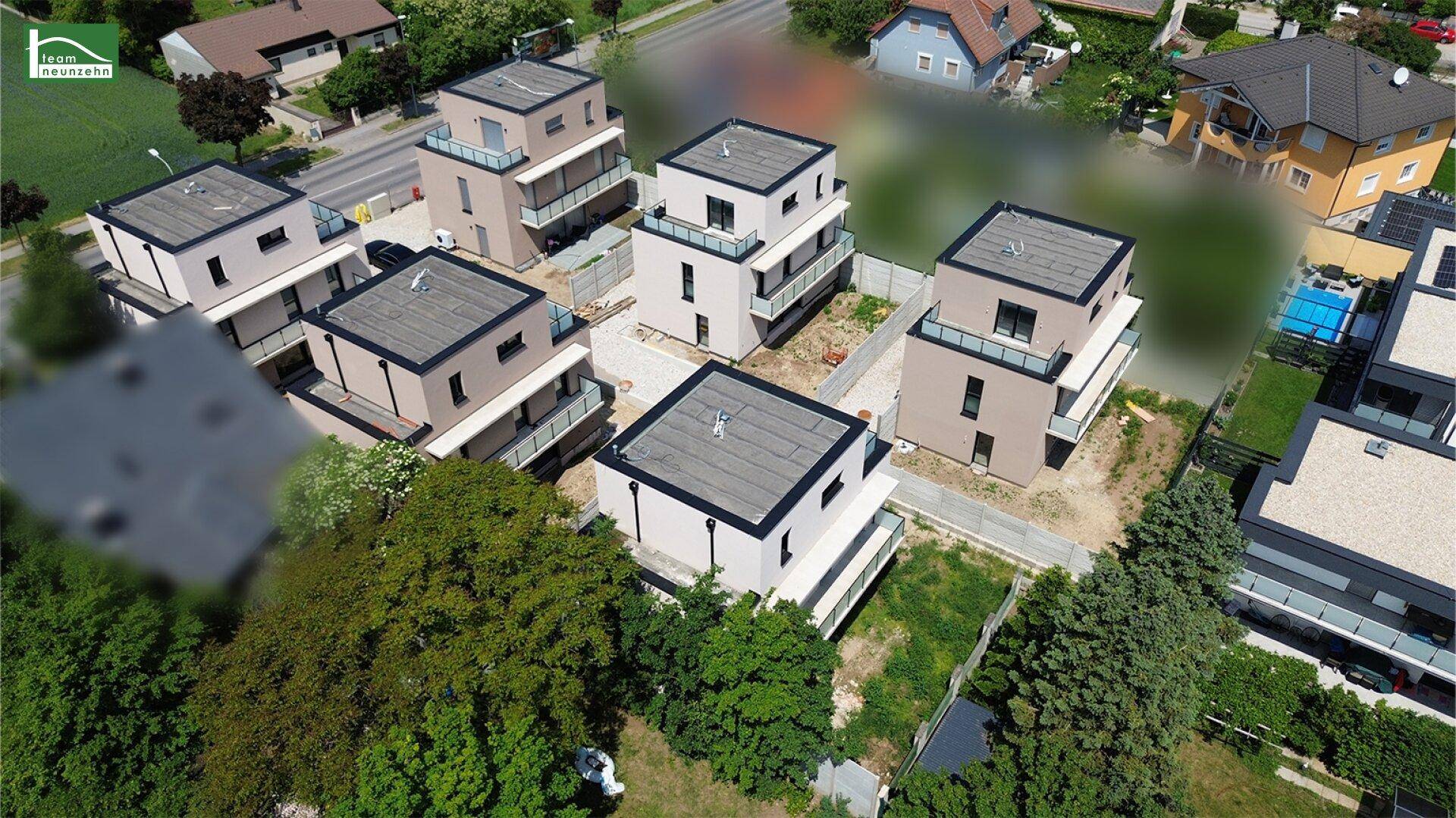 Luftaufnahme einer Gruppe von modernen Neubauten mit Flachdächern in einer grünen Umgebung.