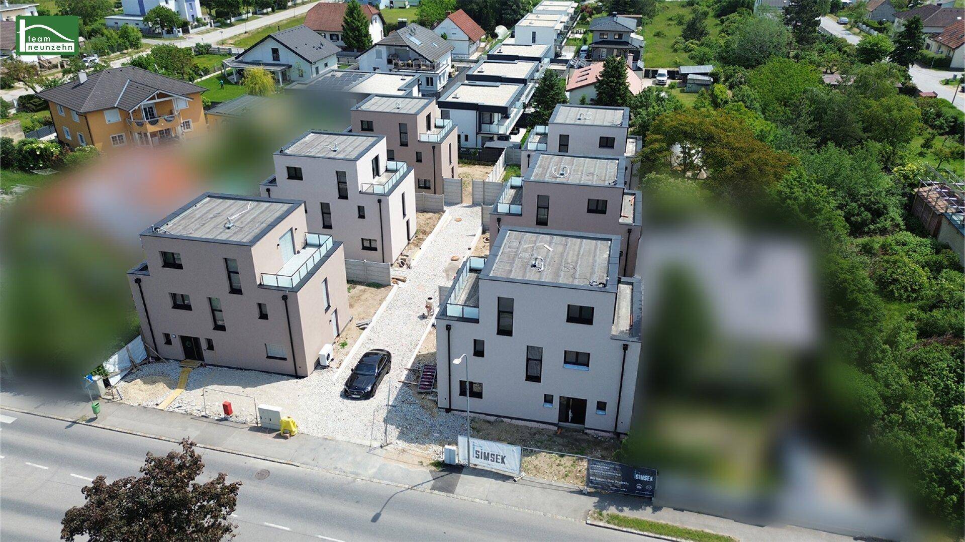 Vogelperspektive auf eine Reihe moderner Häuser entlang einer Straße mit grüner Umgebung.