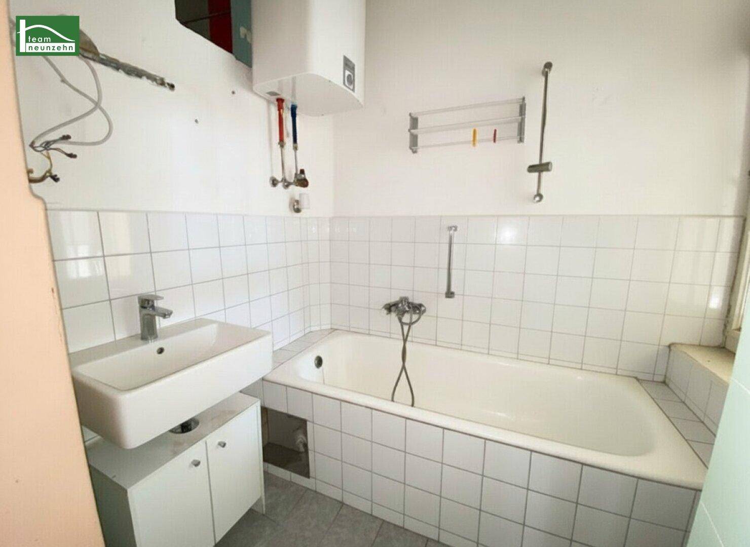 Badezimmer mit Badewanne, Waschbecken und weißen Fliesen, das eine Renovierung benötigt.