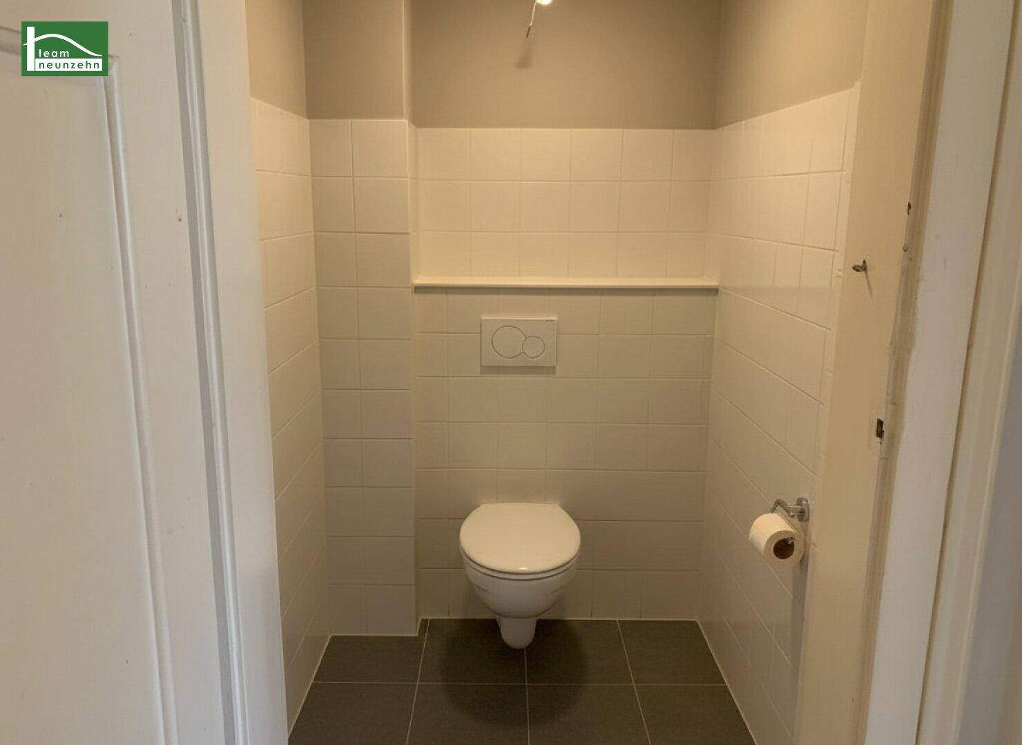 Kleines Gäste-WC mit wandhängender Toilette und modernen Fliesen an Wänden und Boden.