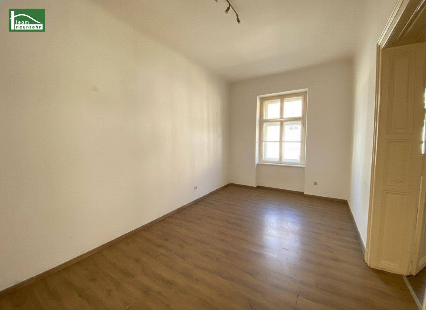 Heller, leerer Raum mit Laminatboden und einem Fenster, das den Raum mit Licht füllt.
