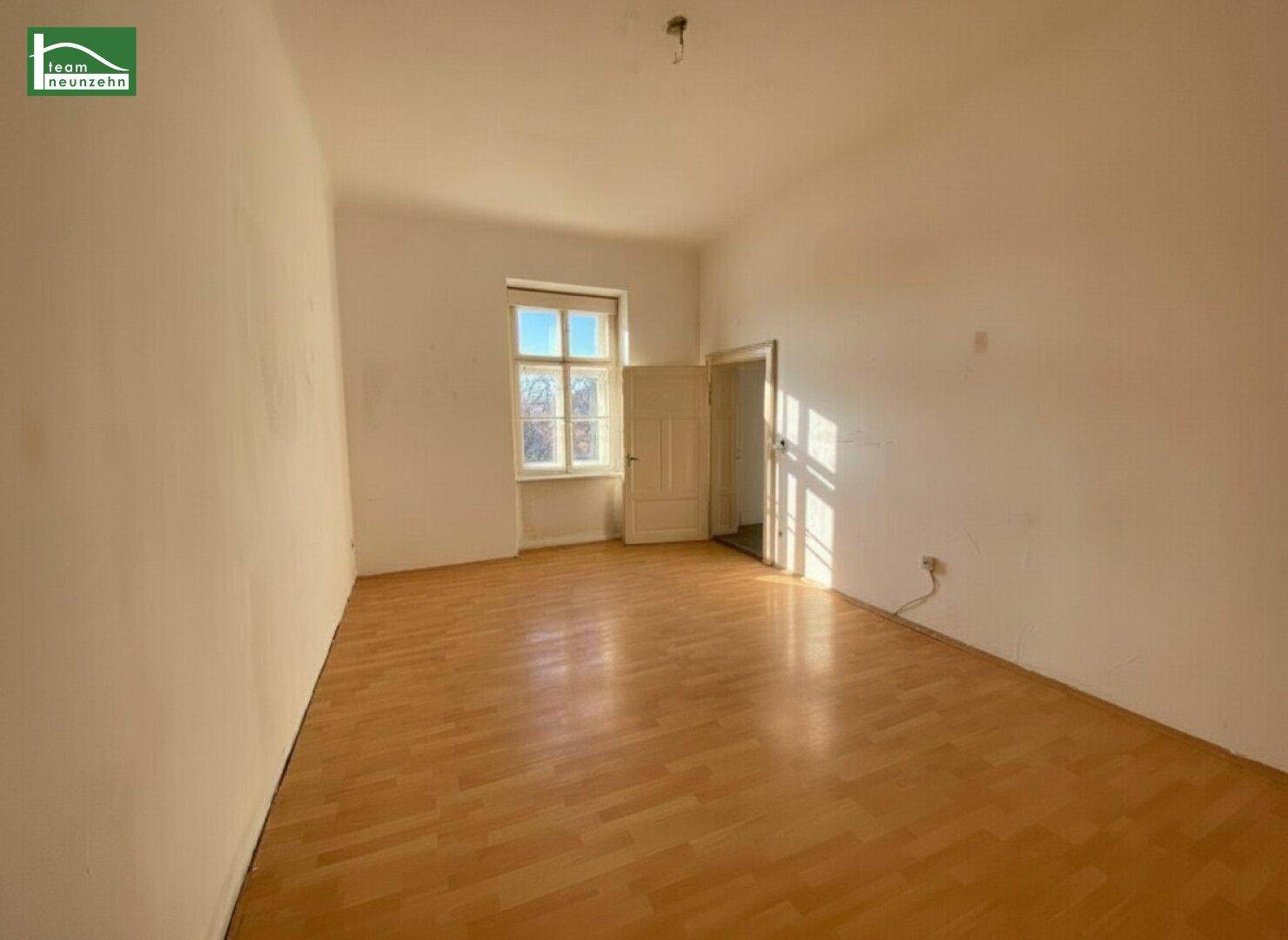 Sonniger, leerer Raum mit hellem Laminatboden und einem Fenster, das viel Licht hereinlässt.