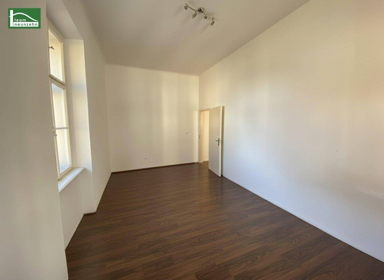 Leerer Raum mit Laminatboden und einem Fenster, das viel Tageslicht hereinlässt.