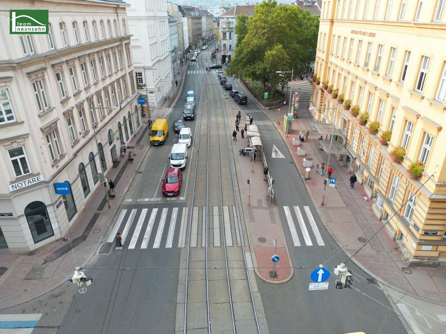 Blick von oben auf eine belebte Stadtstraße mit historischen Gebäuden und Straßenbahnschienen.