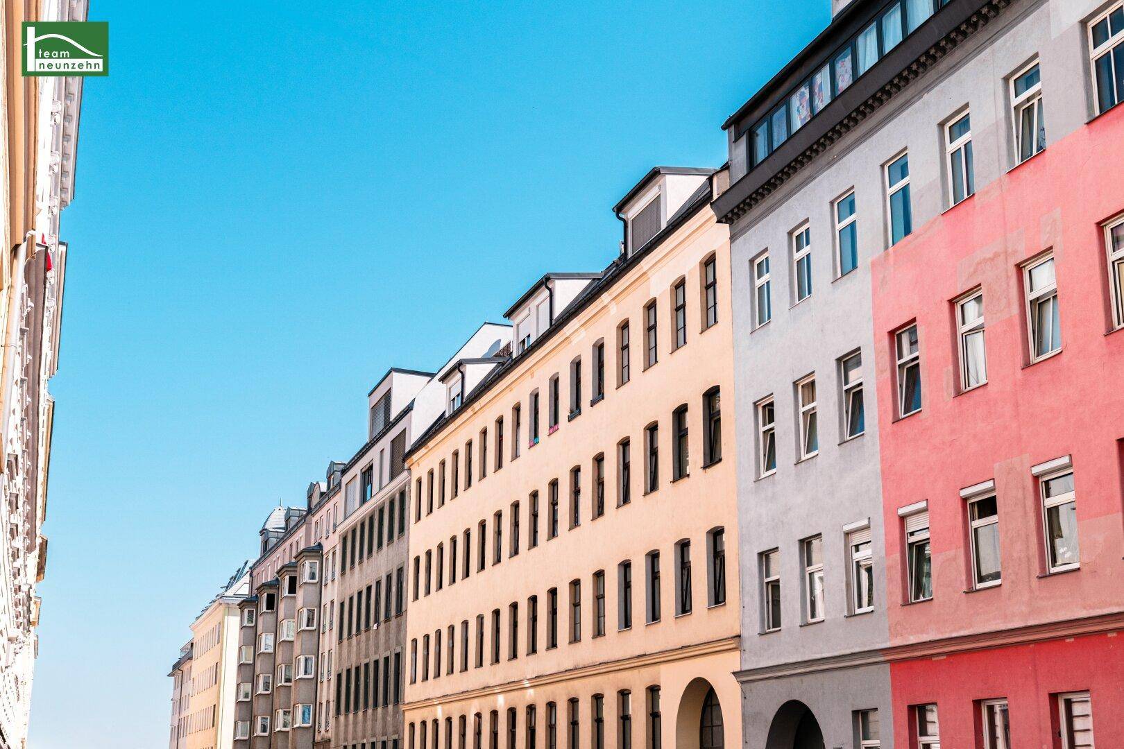Farbige Fassaden von Mehrfamilienhäusern entlang einer städtischen Straße unter klarem Himmel.