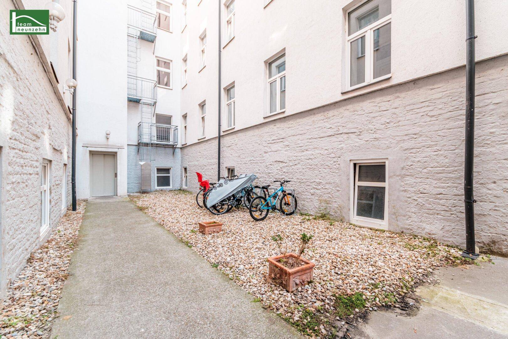 Ruhiger Innenhof mit Kiesfläche und Abstellmöglichkeiten für Fahrräder, umgeben von Gebäuden.