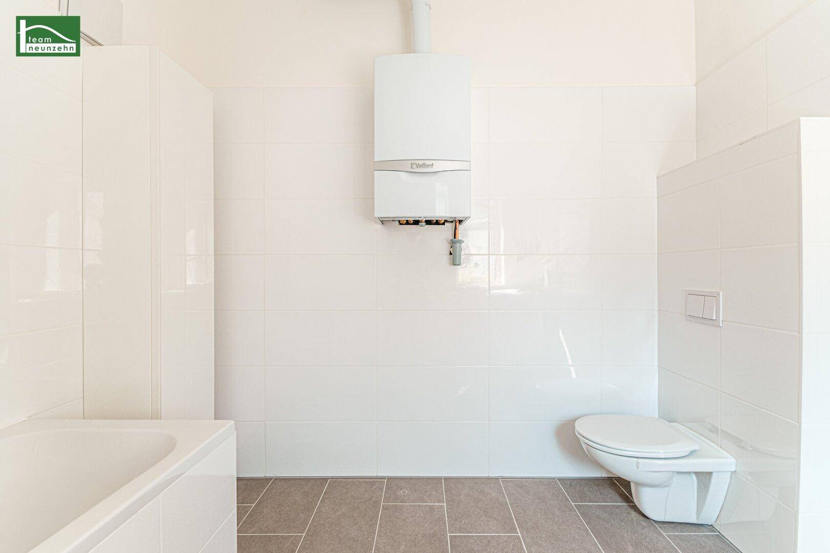 Funktionales Badezimmer mit wandhängendem WC und Gastherme, alles in hellen Fliesen gehalten.