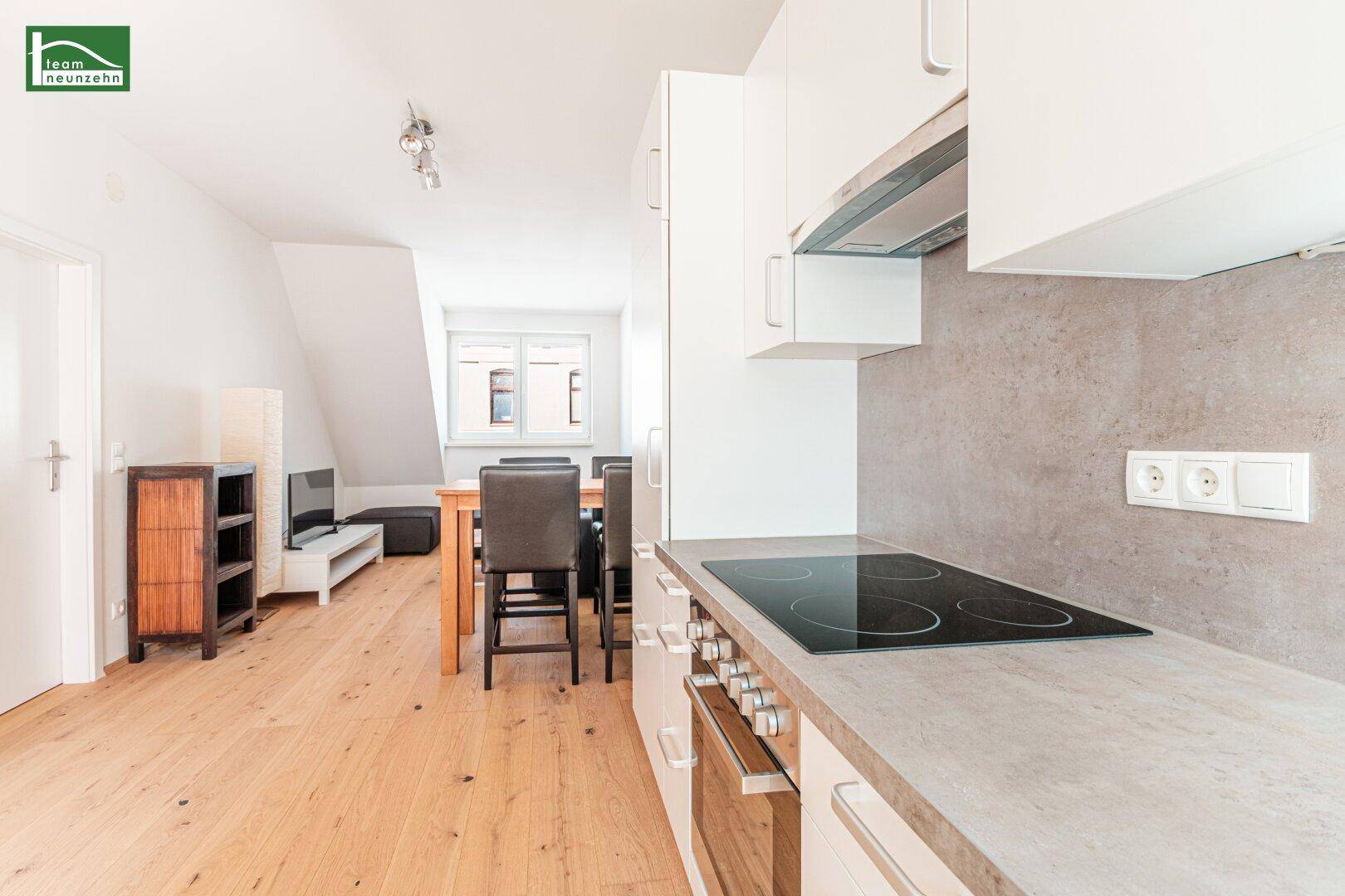 Moderne Küchenzeile mit heller Arbeitsplatte, Kochfeld und Blick in den offenen Wohnbereich.