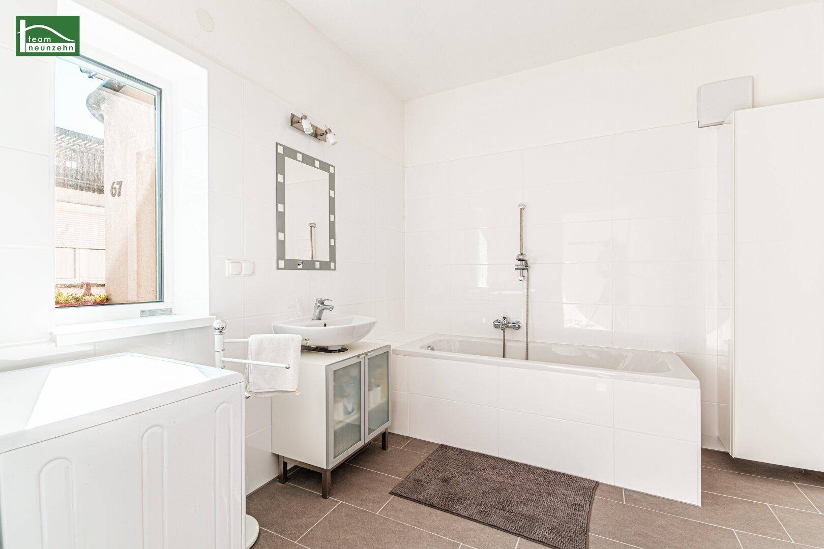 Helles Badezimmer mit Badewanne, Waschbecken, Waschmaschine und Fenster für gute Belüftung.