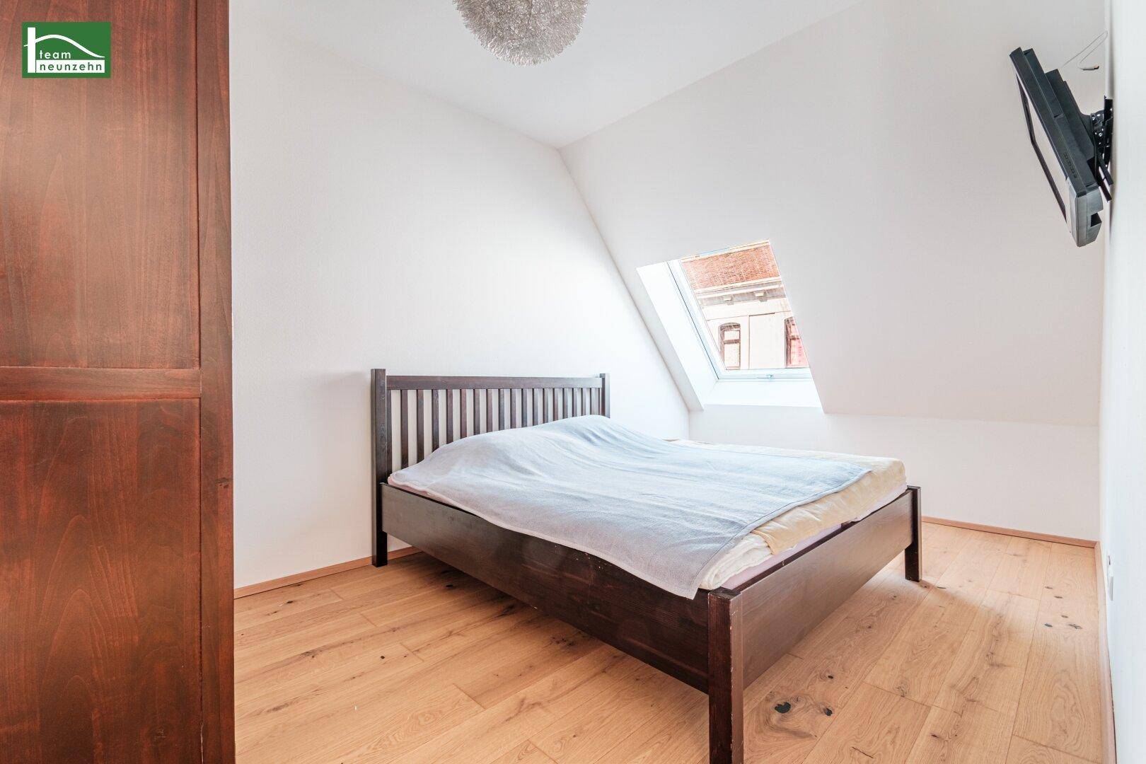 Gemütliches Schlafzimmer mit Holzbett, Dachfenster und schrägen Wänden für eine besondere Atmosphäre.