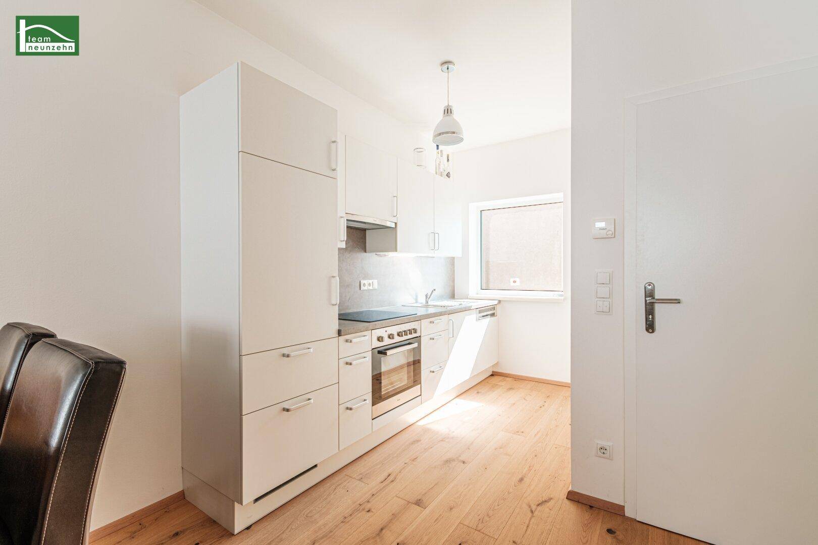 Funktionale Einbauküche mit weißen Schränken, integriertem Backofen und Fenster für Tageslicht.