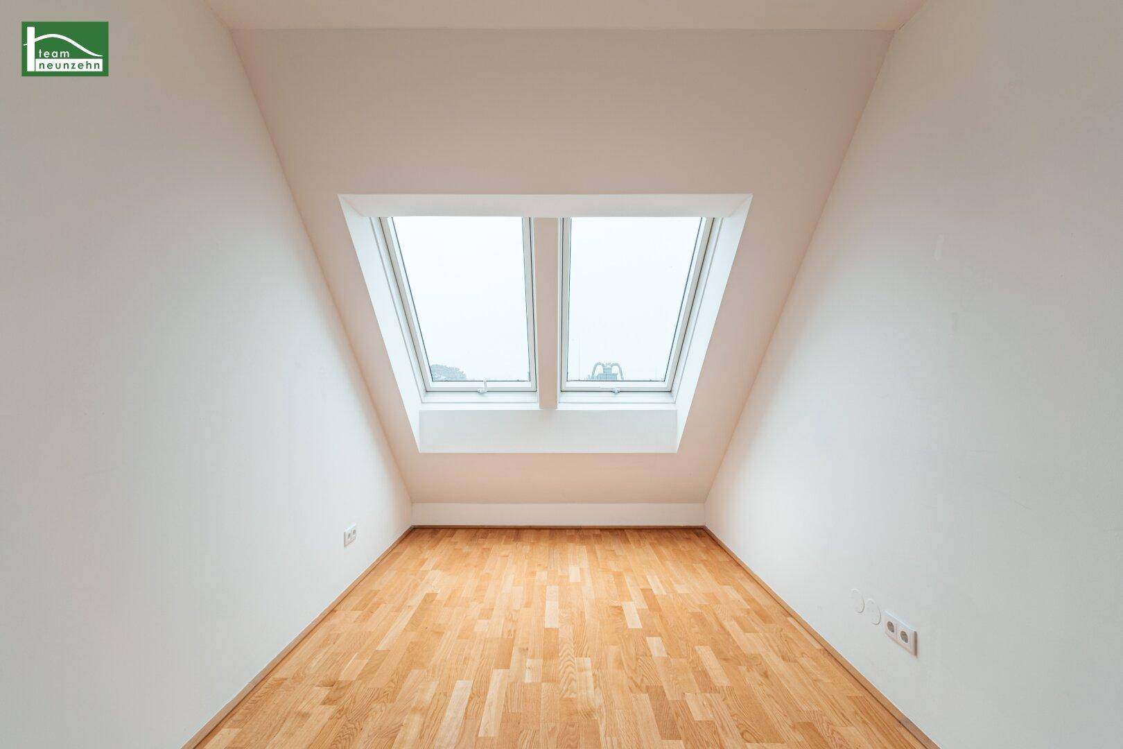 Helles Zimmer im Dachgeschoss mit Schrägdach und zwei großen Dachfenstern.