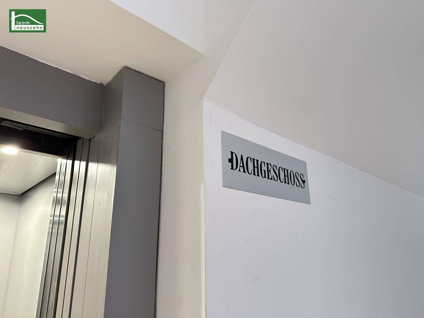 Moderner Aufzugsbereich mit weißer Wand und Beschilderung zum Dachgeschoss.