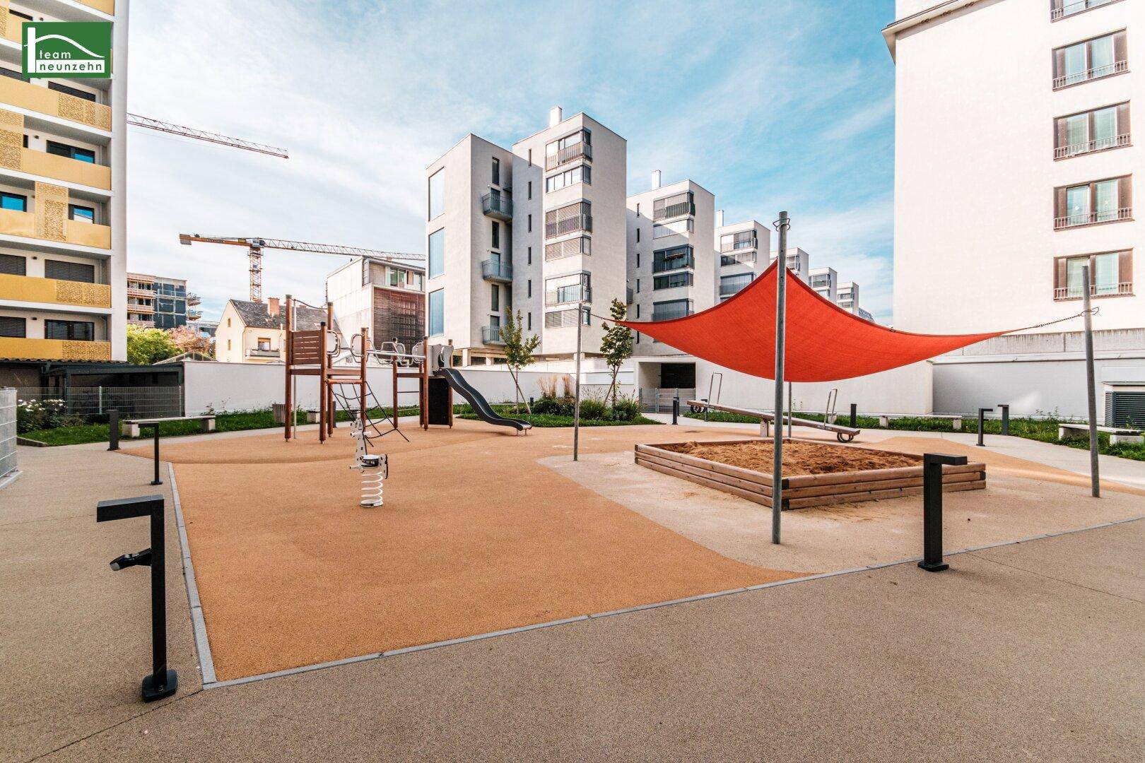 Moderner Kinderspielplatz mit Sandkasten, Rutsche und Sonnensegel in der Wohnanlage.