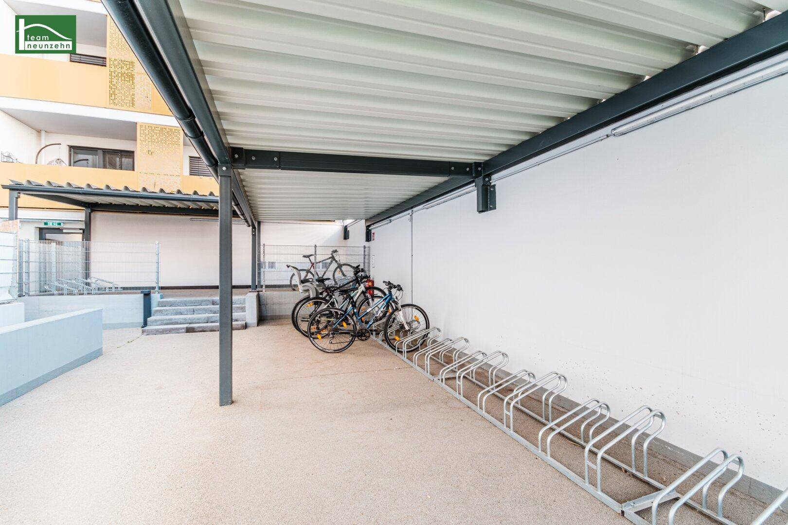 Überdachter Fahrradabstellplatz mit mehreren Fahrradständern neben dem Gebäude.