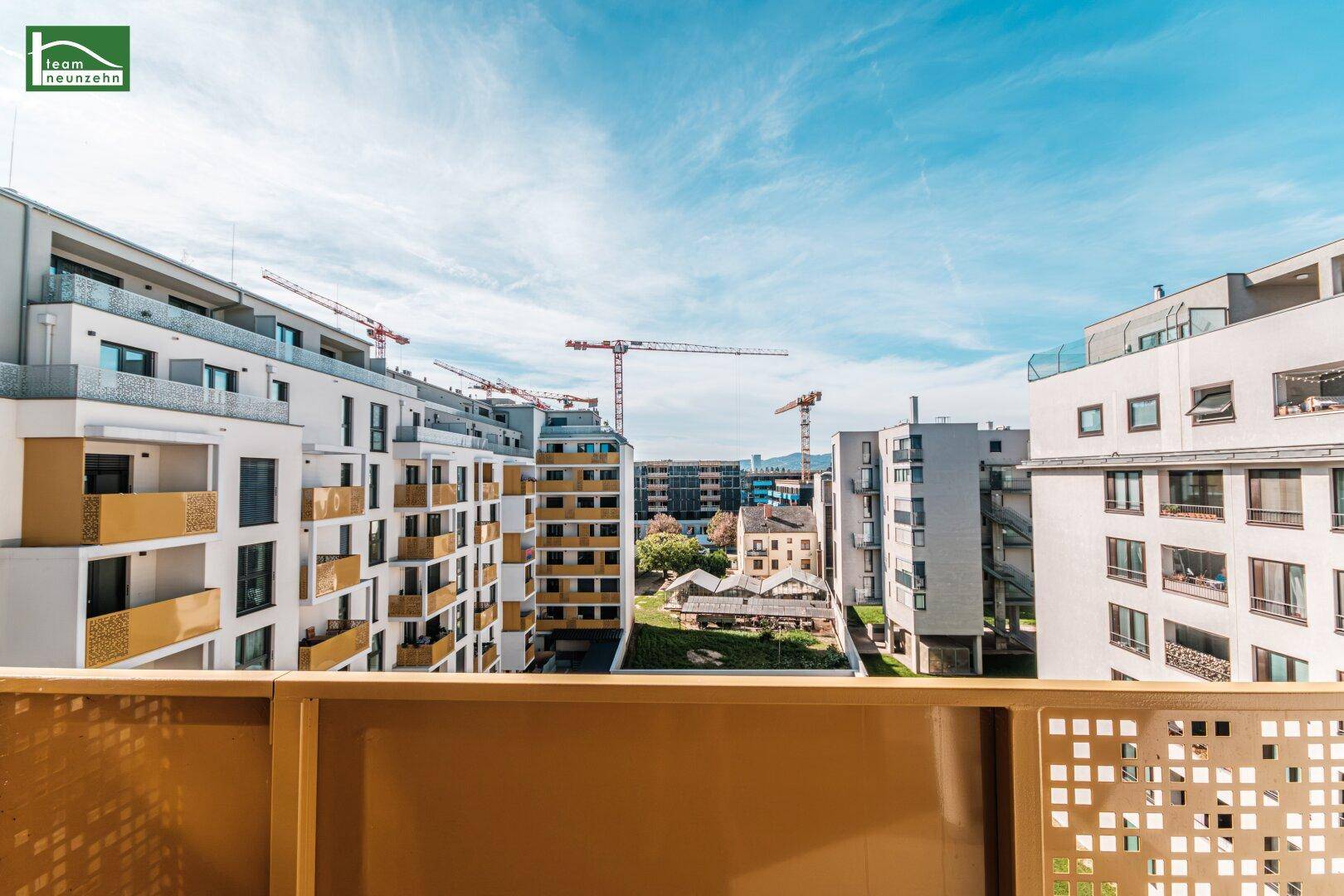 Weitblick von einem Balkon über die umliegende Wohngegend mit Baukränen am Horizont.