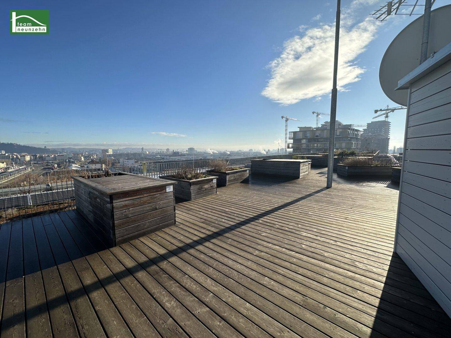 Weitläufige Dachterrasse mit Holzdielen und Panoramablick über die Stadt.