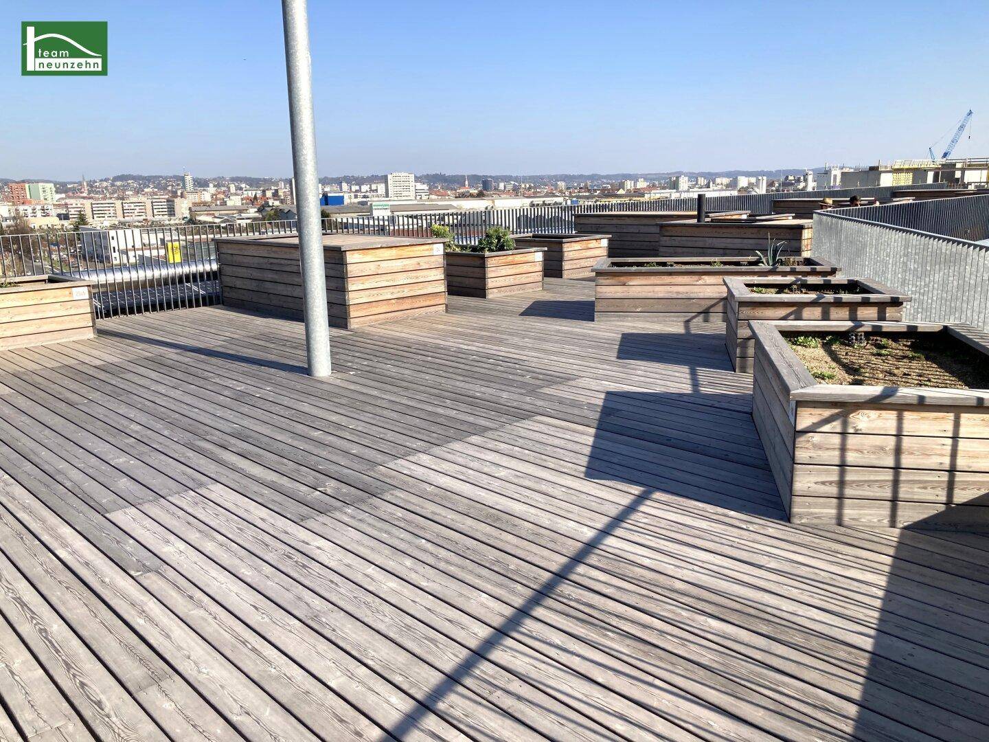 Große Dachterrasse mit Holzboden und Pflanzbeeten, bietet weiten Stadtblick.