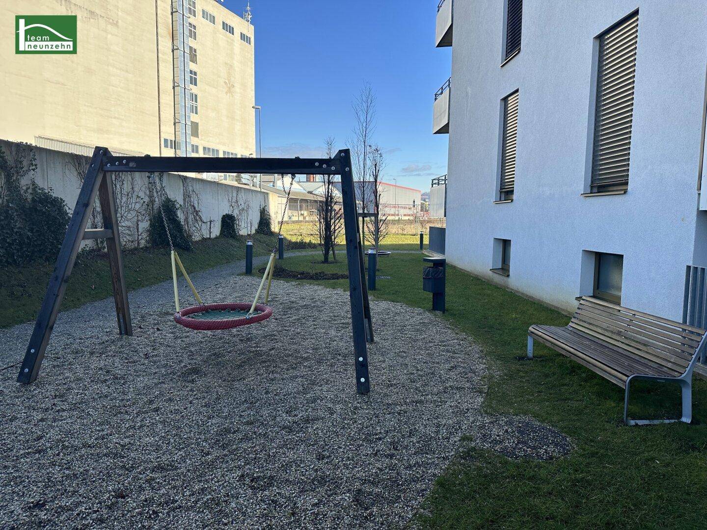 Kleiner Spielplatz mit Schaukel und Sitzbank im Außenbereich der Wohnanlage.