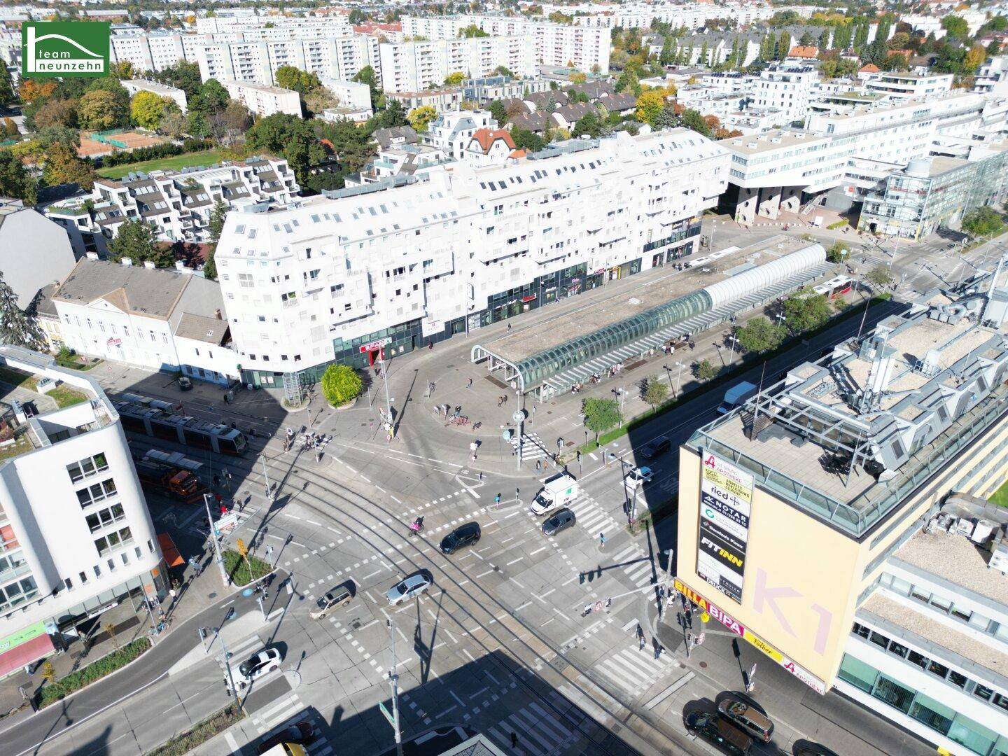 Luftaufnahme einer belebten Stadtkreuzung mit Straßenbahnschienen und umliegenden Wohngebäuden.