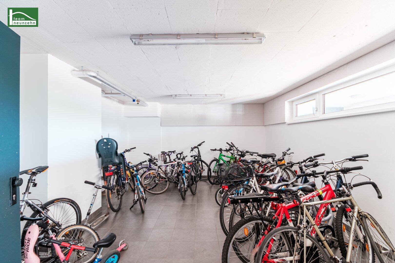 Geräumiger Fahrradraum mit zahlreichen Fahrrädern, praktischem Fliesenboden und einem Fenster für natürliche Belichtung.