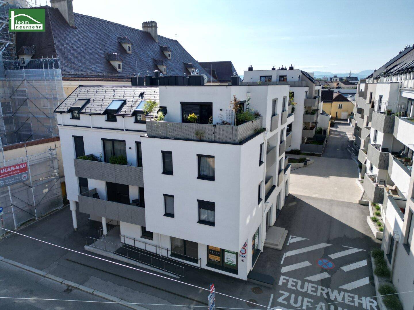 Zeitgenössisches Wohngebäude mit weißer Fassade, Balkonen und einer begrünten Dachterrasse in urbaner Lage.