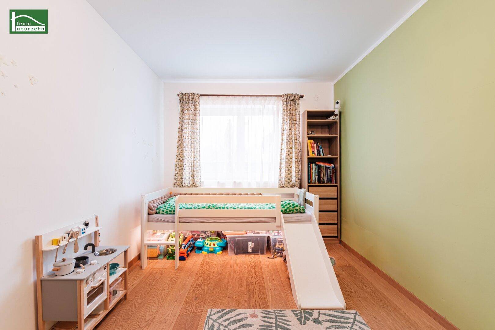 Helles Kinderzimmer mit Spielbett, Bücherregal und Blick ins Grüne durch das Fenster.