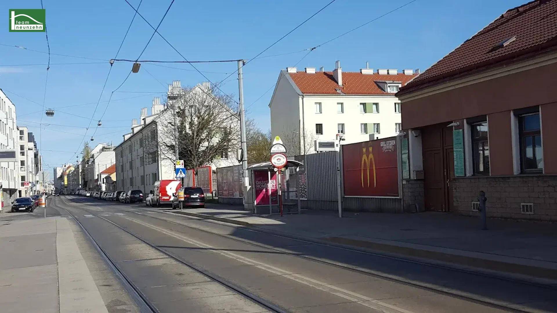 Belebte Stadtstraße mit Straßenbahnschienen, Bushaltestelle und umliegenden Gebäuden.