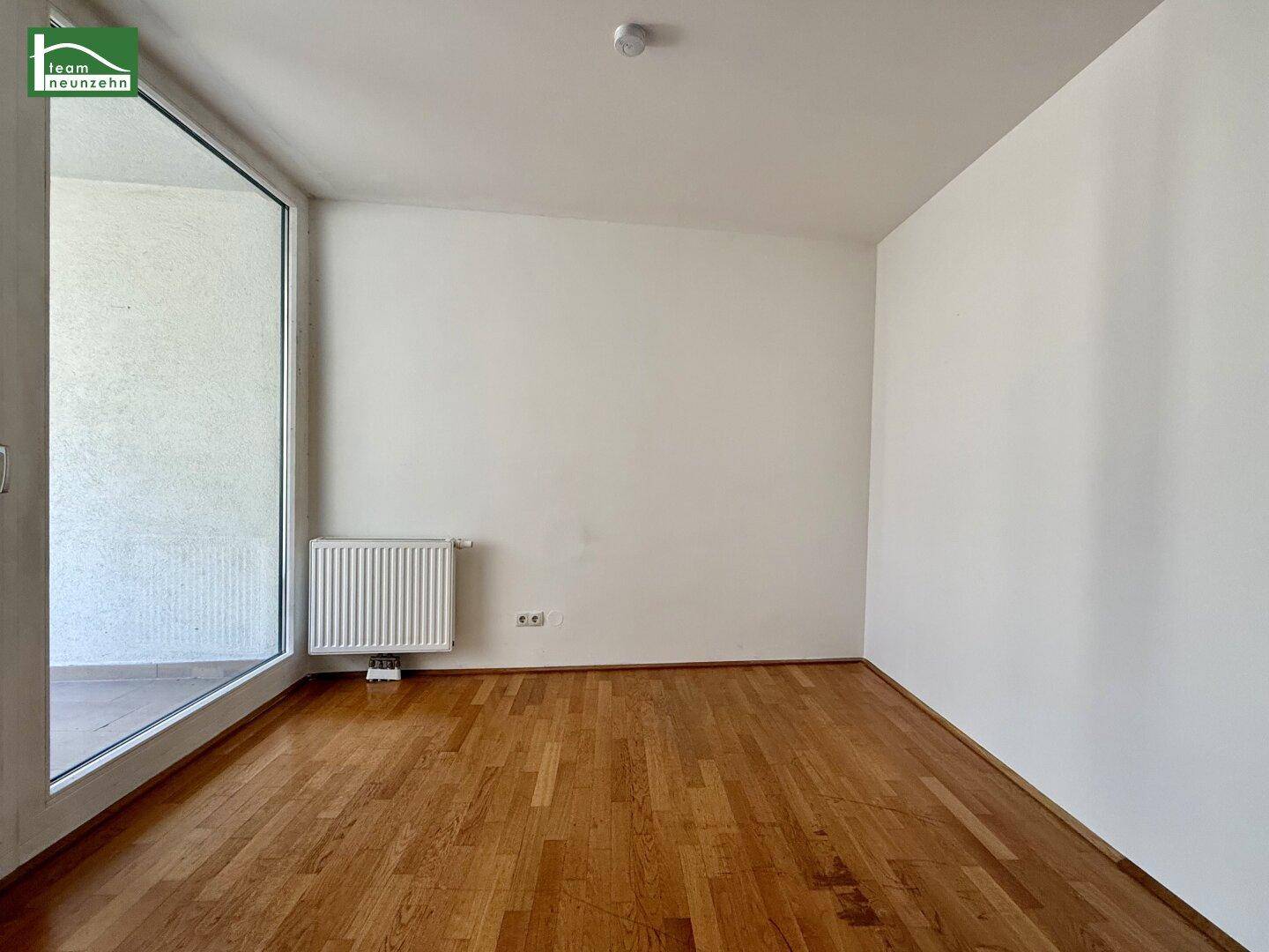 Geräumiges Schlafzimmer mit Parkettboden und großer Fensterfront, die zum Balkon führt.