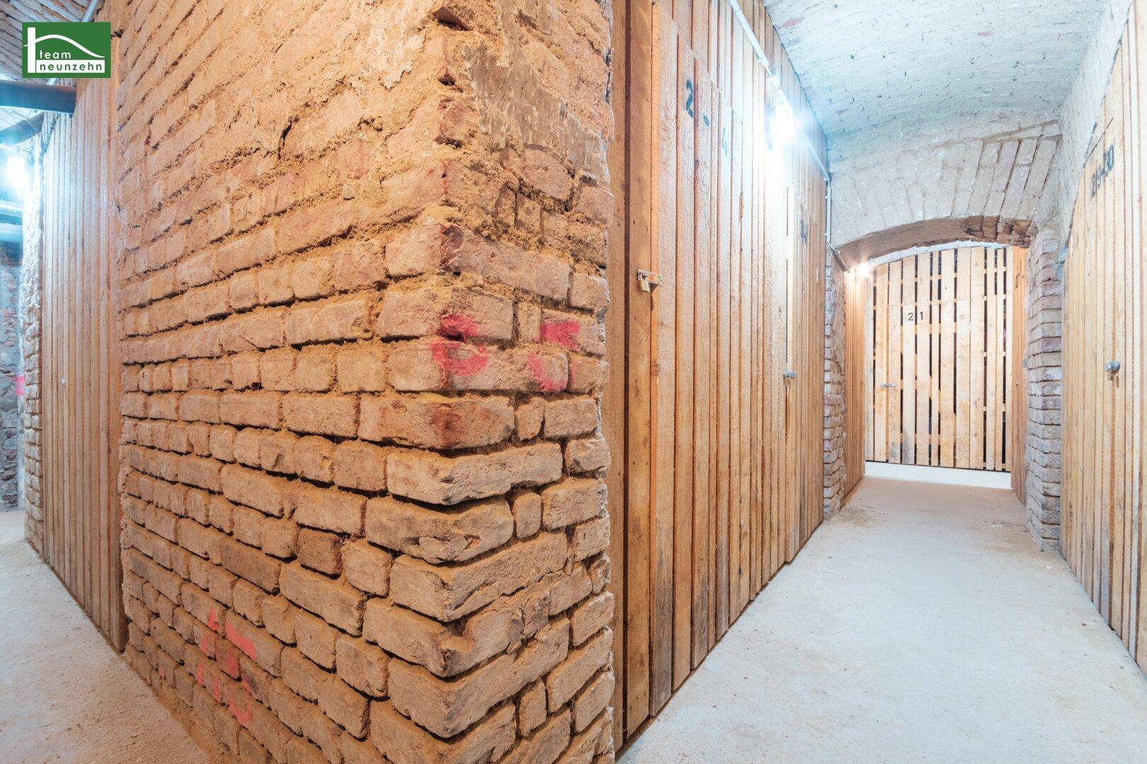 Kellerabteil mit unverputzten Ziegelwänden und Holzverschlägen für zusätzlichen Stauraum.