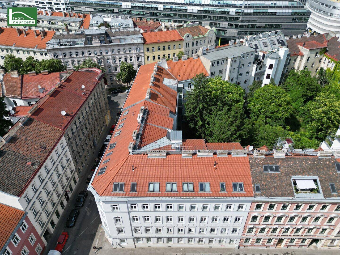 Luftaufnahme eines Wohnblocks mit rotem Ziegeldach und begrüntem Innenhof in der Stadt.
