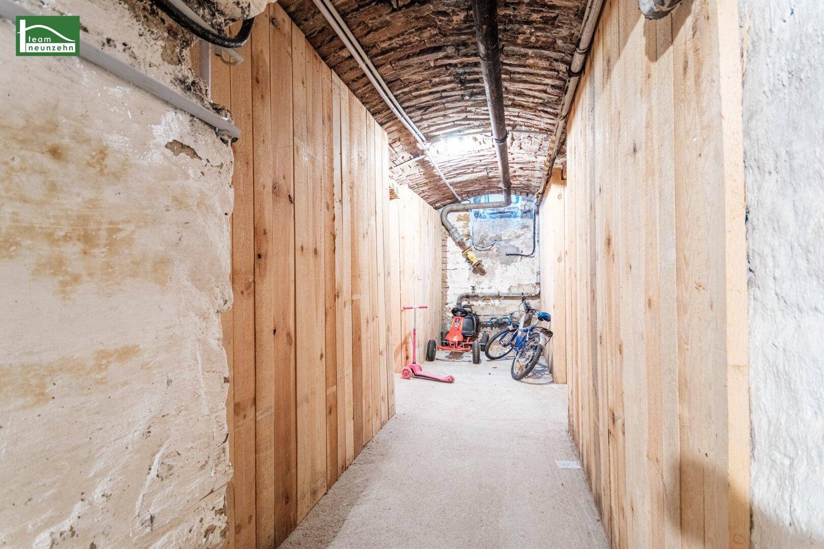 Kellergang mit Holzverkleidung an den Wänden und sichtbaren Rohren an der Decke.