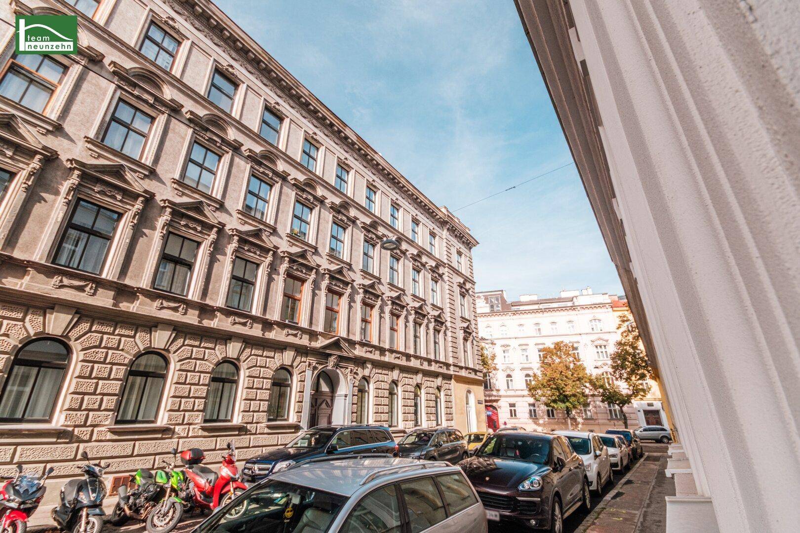 Historisches Gebäude mit reich verzierten Fassaden und parkenden Autos auf der Straße.