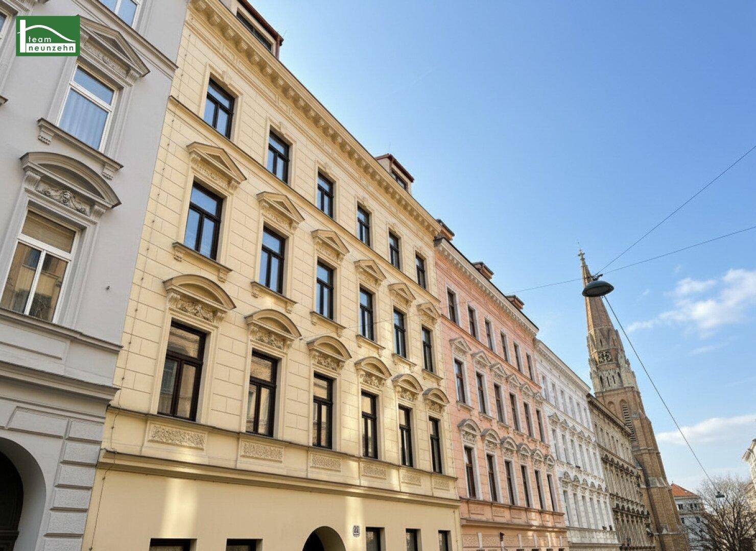 Historische Gebäudezeile mit dekorativen Fassaden und einem Kirchturm im Hintergrund.