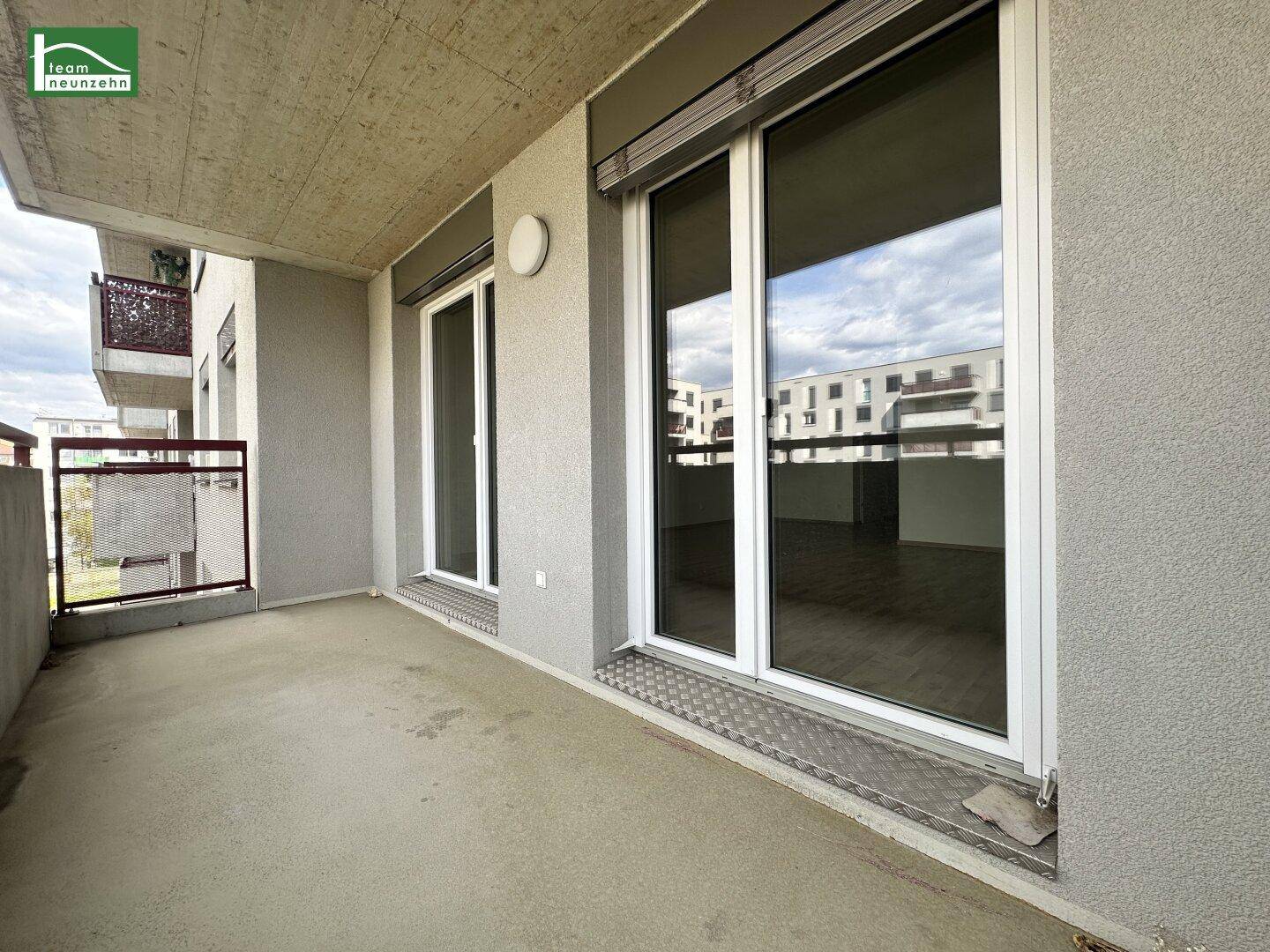 Geräumiger Balkon mit Betonboden, Blick auf die umliegenden Gebäude und Rollläden an den Fenstern.