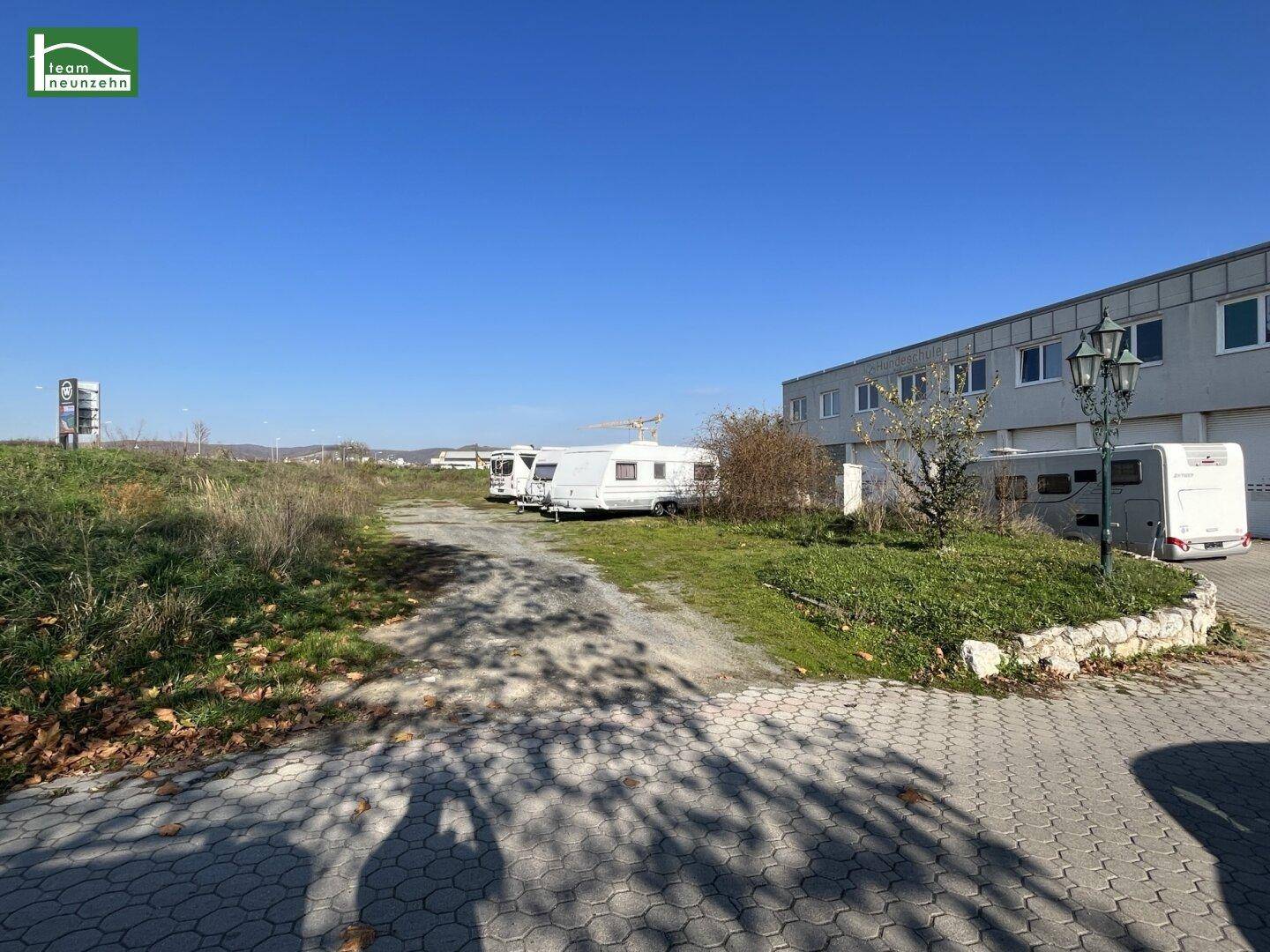 Außenansicht eines Gewerbegebiets mit einem Gebäude, Parkplätzen und abgestellten Wohnwagen unter blauem Himmel.