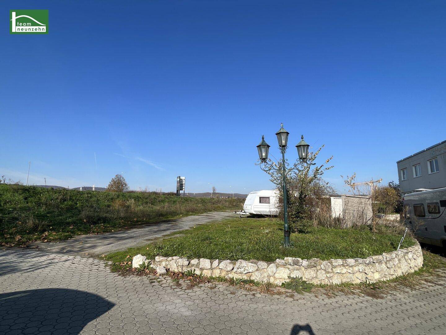 Blick auf einen gepflasterten Bereich mit einer dekorativen Laterne, umgeben von Grünflächen und einem Gebäude im Hintergrund.