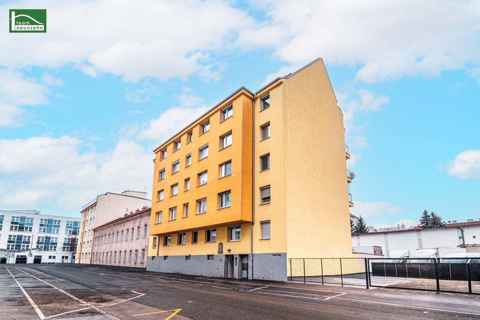 Gelbes Mehrfamilienhaus mit mehreren Stockwerken und zahlreichen Fenstern unter blauem Himmel.