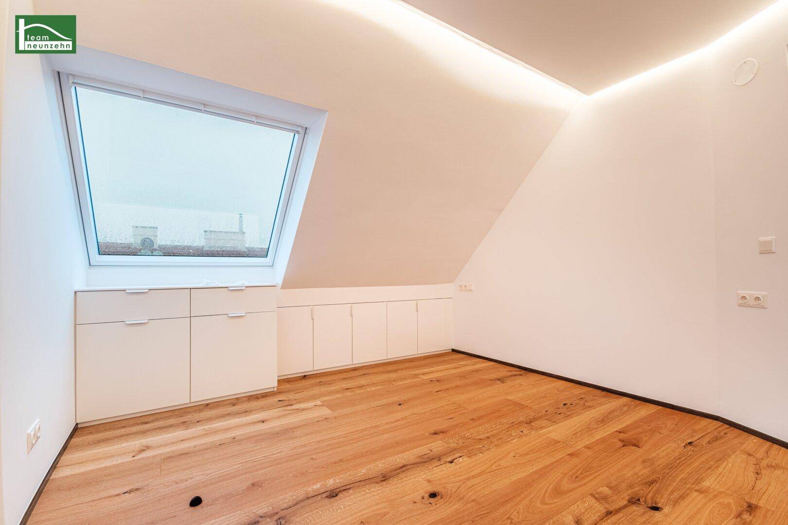 Geräumiges Zimmer im Dachgeschoss mit Holzboden, Dachfenster und niedrigen Einbauschränken.