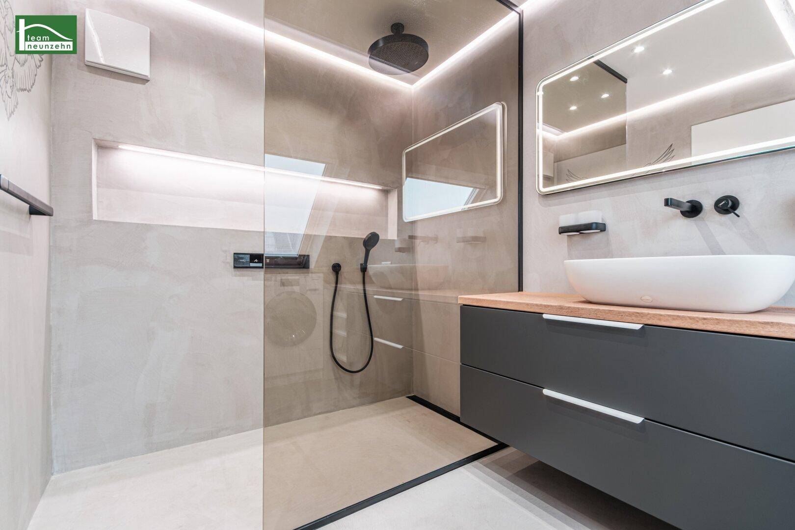 Elegantes Badezimmer mit begehbarer Dusche, modernen Armaturen und beleuchtetem Spiegel.