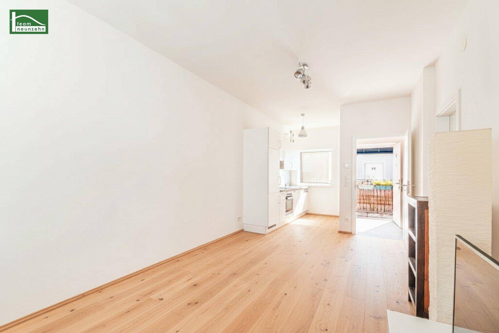 Offener Wohnbereich mit Küchenzeile und Zugang zu einem sonnigen Balkon.