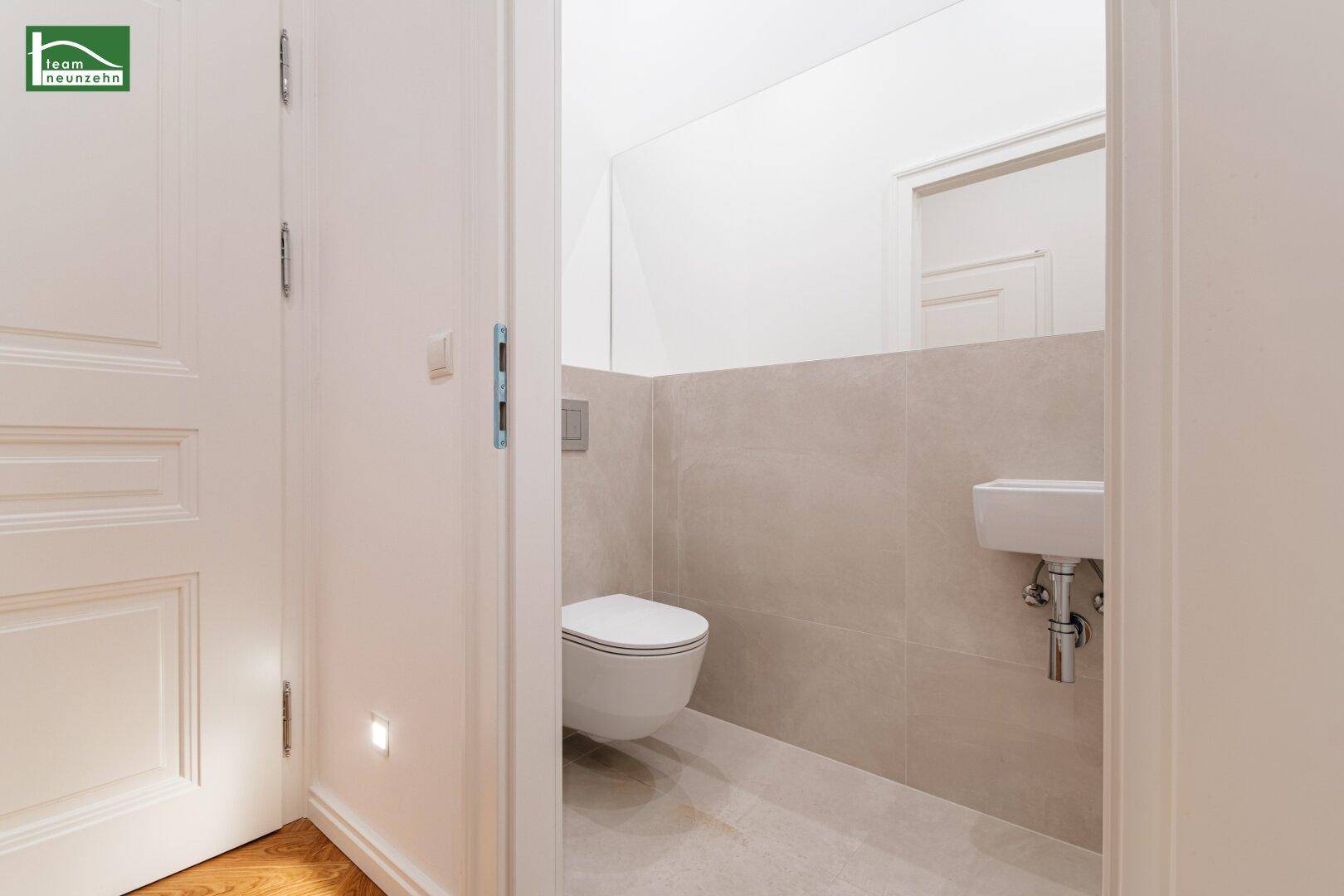 Kompaktes Gäste-WC mit wandhängender Toilette und kleinem Handwaschbecken, modern gefliest.