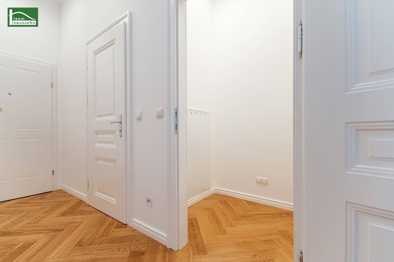 Heller Flur mit Fischgrätparkett und einem offenen Zugang zu einem kleinen Abstellbereich.