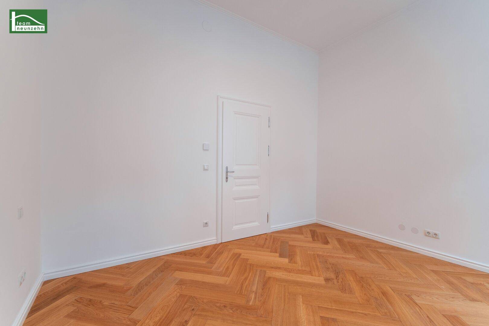 Leeres Zimmer mit Fischgrätparkett und einer weißen Tür, bereit zur individuellen Gestaltung.