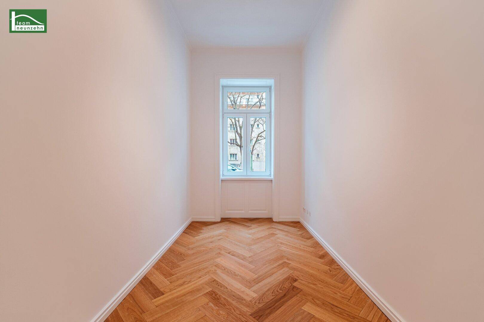 Kleines, helles Zimmer mit Fischgrätparkettboden und einem Fenster mit Blick ins Grüne.