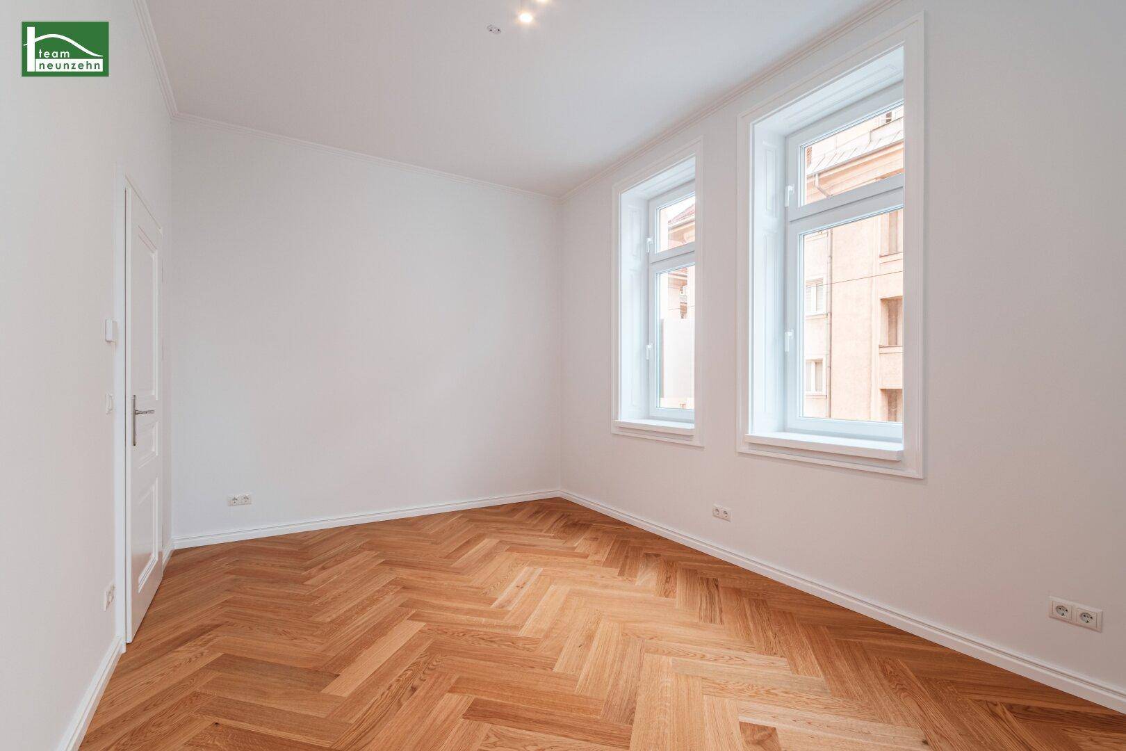 Geräumiges Zimmer mit Fischgrätparkett und zwei großen Fenstern, ideal als Schlaf- oder Arbeitszimmer.