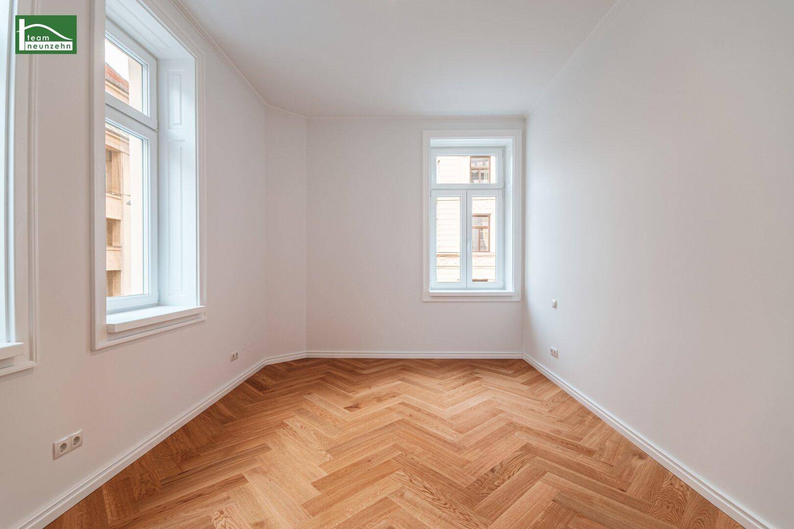 Ruhiges Schlafzimmer mit elegantem Fischgrätparkett und zwei Fenstern für viel Tageslicht.